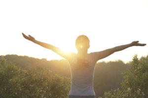 woman with arms raised out looking at the sun
